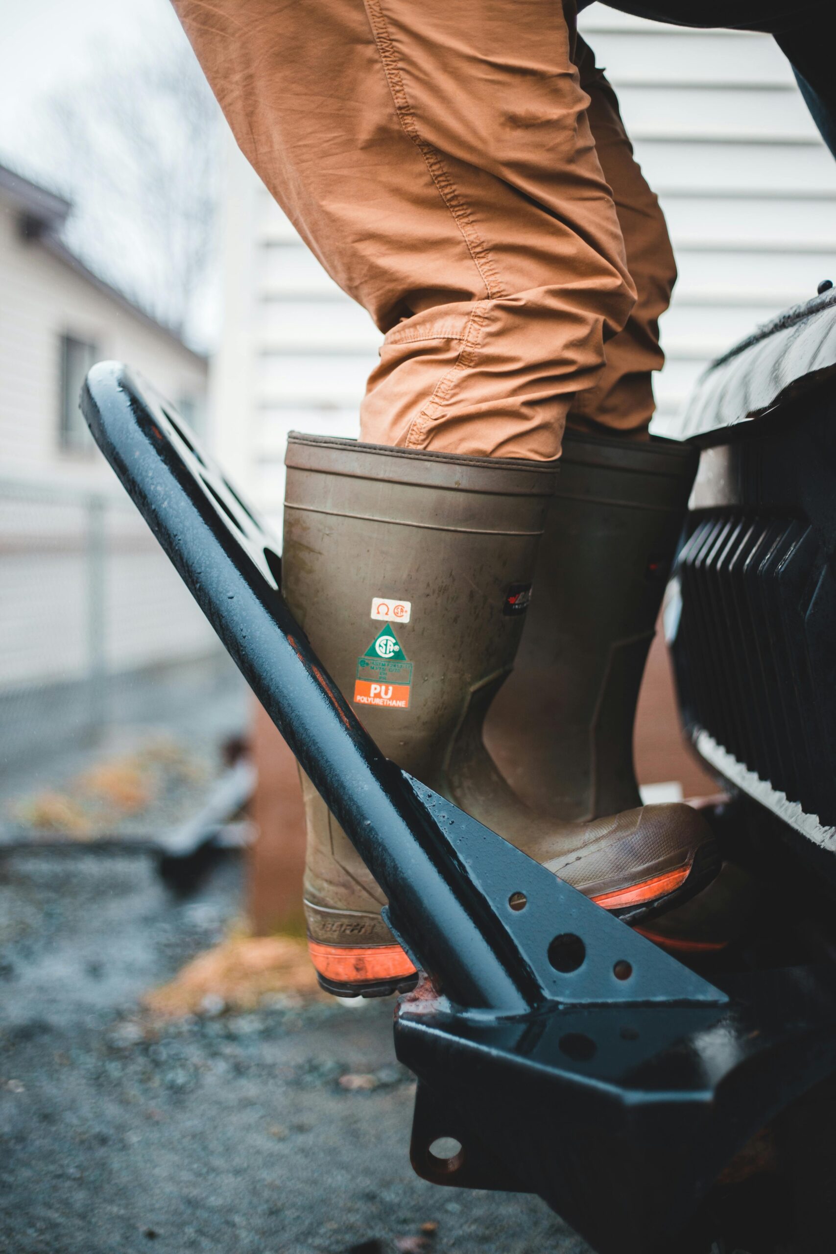 Mechanic wearing gumboots stepping onto vehicle for repair outdoors.