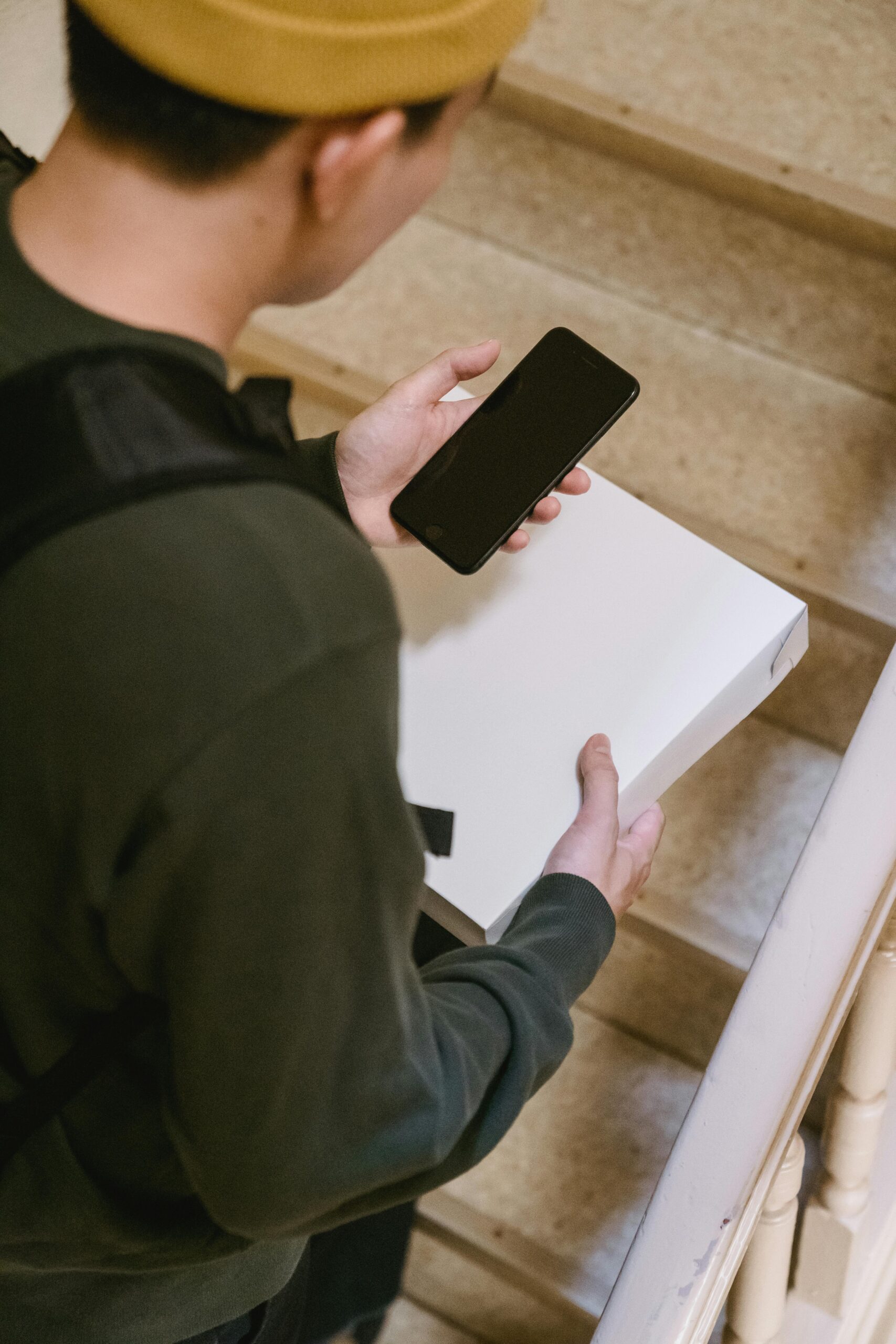 A delivery person checking their phone while holding a package on the stairs.
